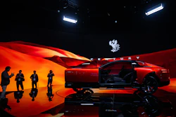Red luxury concept car on stage with dramatic lighting and silhouetted figures