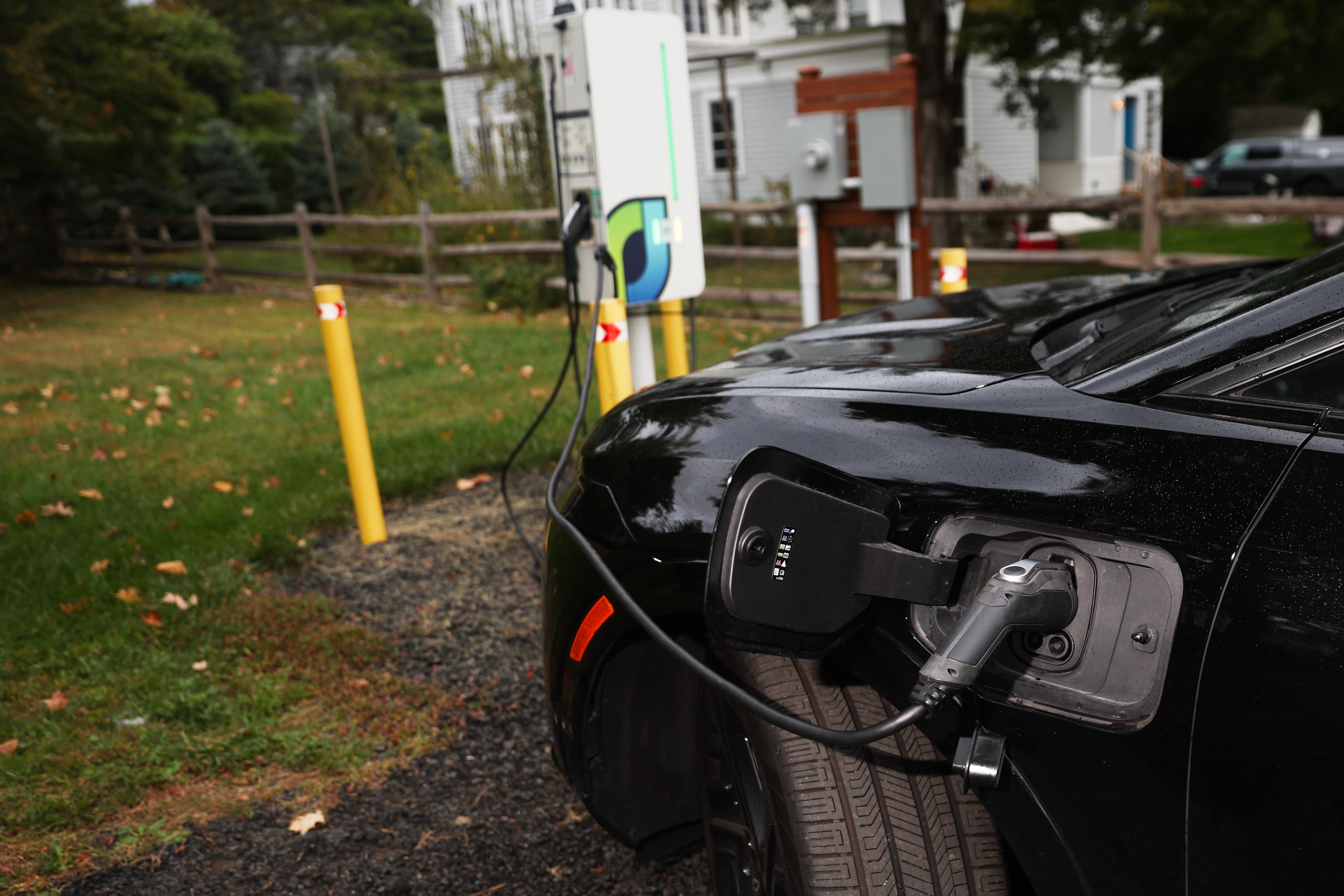 Black electric vehicle charging at outdoor station with green lawn and trees