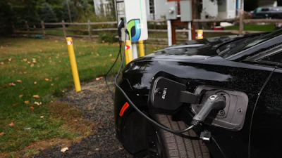 Black electric vehicle charging at outdoor station with green lawn and trees