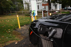 Black electric vehicle charging at outdoor station with green lawn and trees