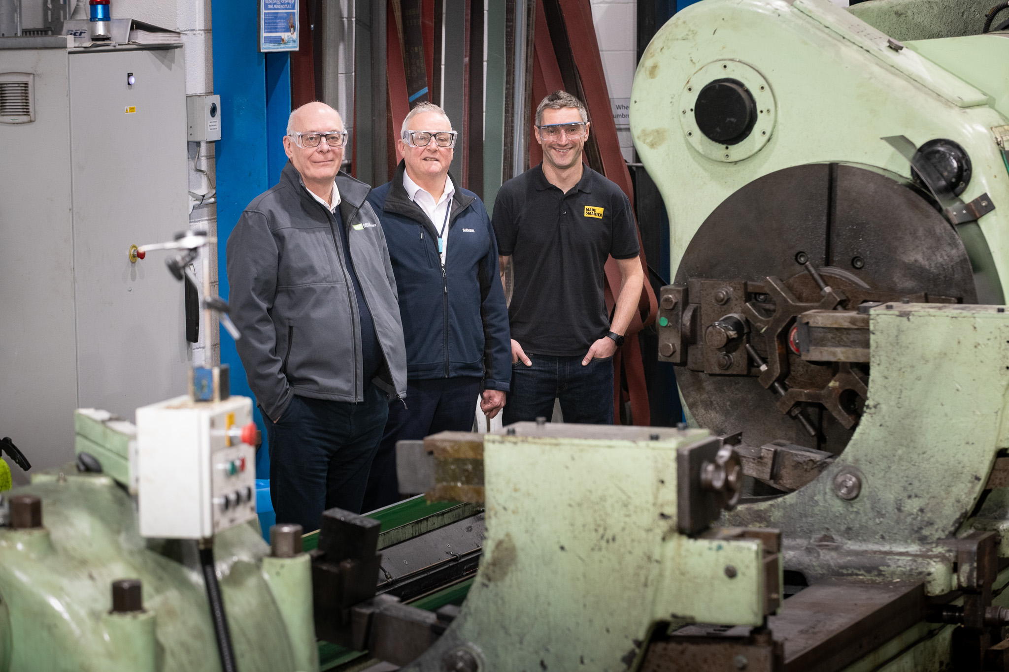 Three workers standing in industrial machine workshop near large mechanical equipment