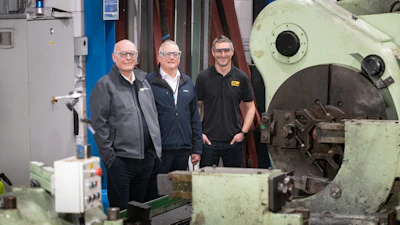 Three workers standing in industrial machine workshop near large mechanical equipment