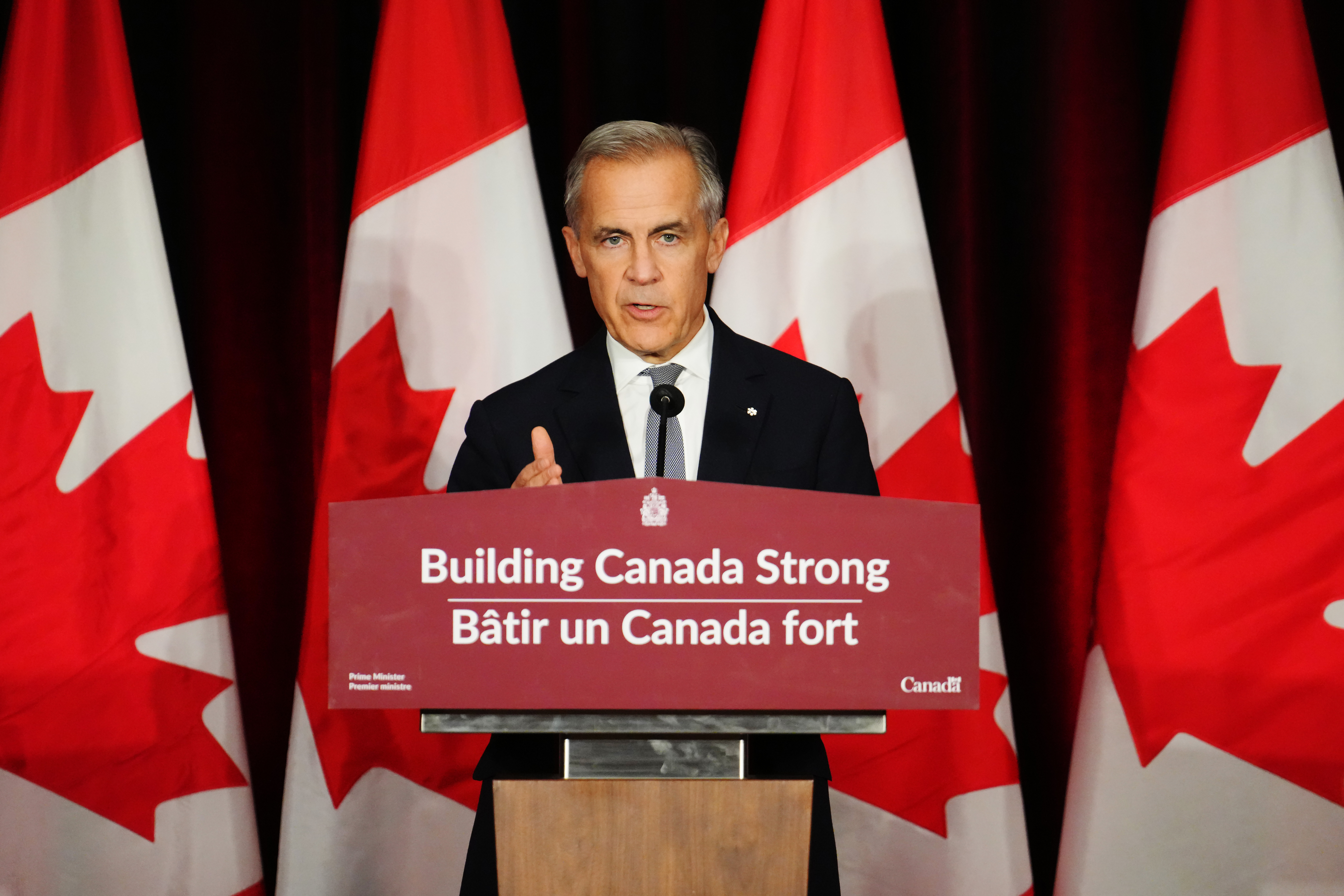 Canadian government official speaking at podium with Canadian flags in background