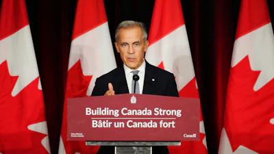 Canadian government official speaking at podium with Canadian flags in background