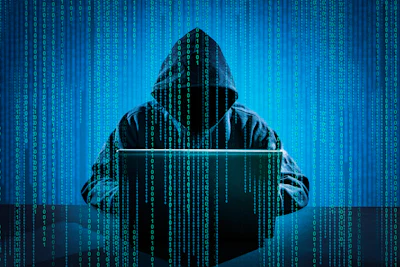 Hooded figure using laptop with digital binary code background