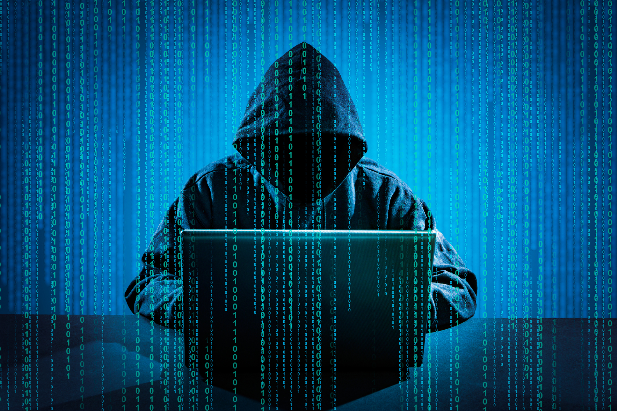 Hooded figure using laptop with digital binary code background