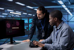 Two cybersecurity professionals analyzing a system hack on a computer monitor