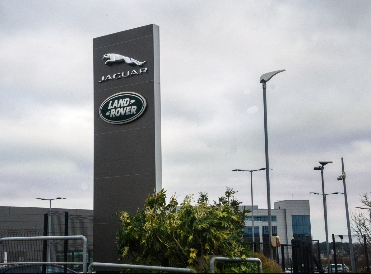 Jaguar Land Rover corporate sign with logos on tall black monolith against cloudy sky