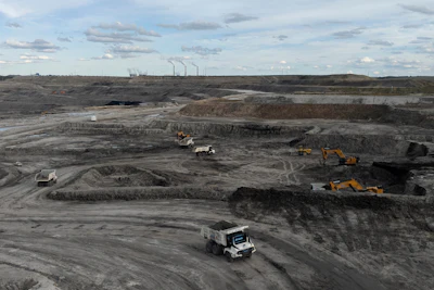 Open-pit coal mine with dump trucks and excavators amid gray landscape and industrial smokestacks
