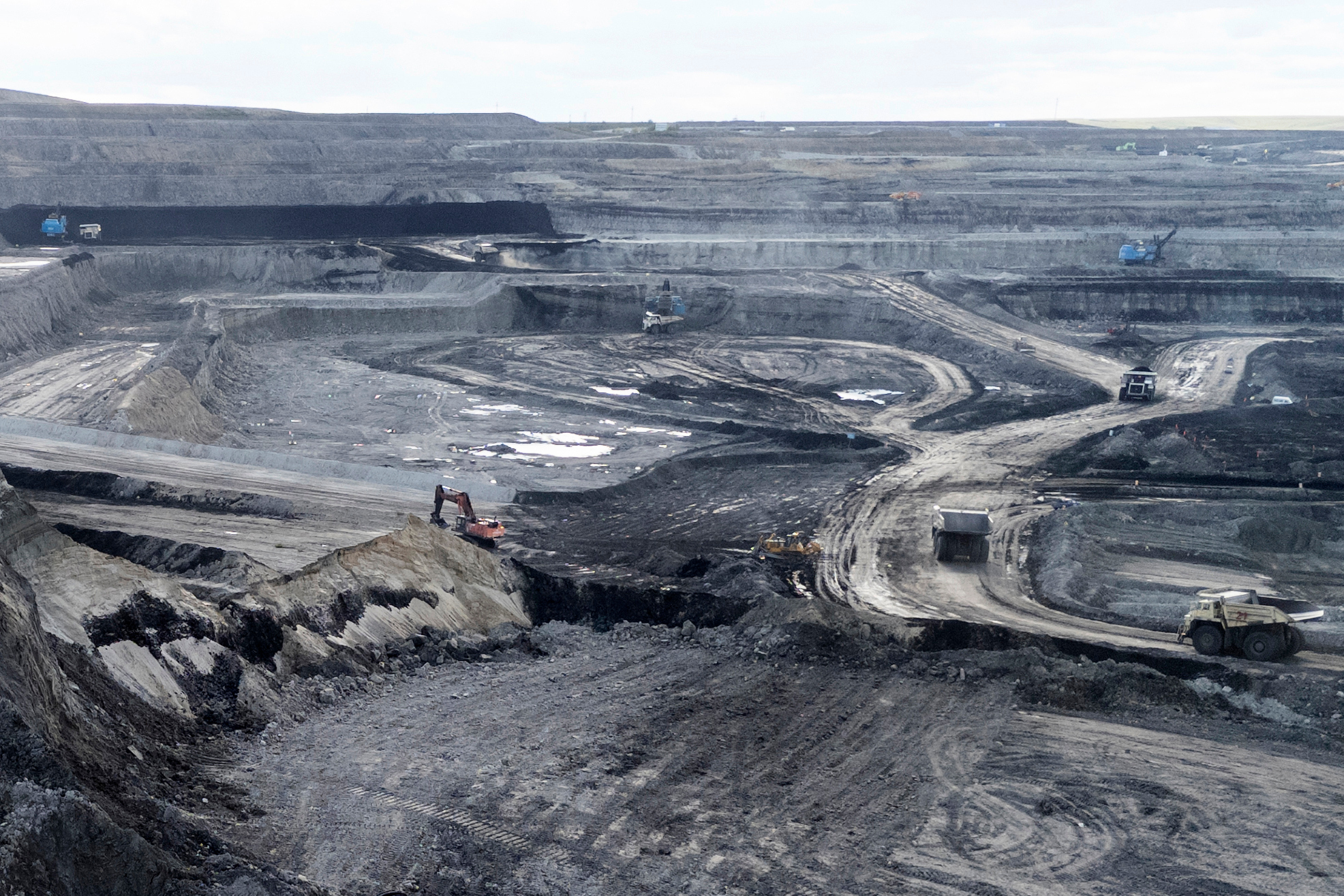 Expansive open-pit coal mine with heavy machinery, layered terrain, and industrial excavation landscape