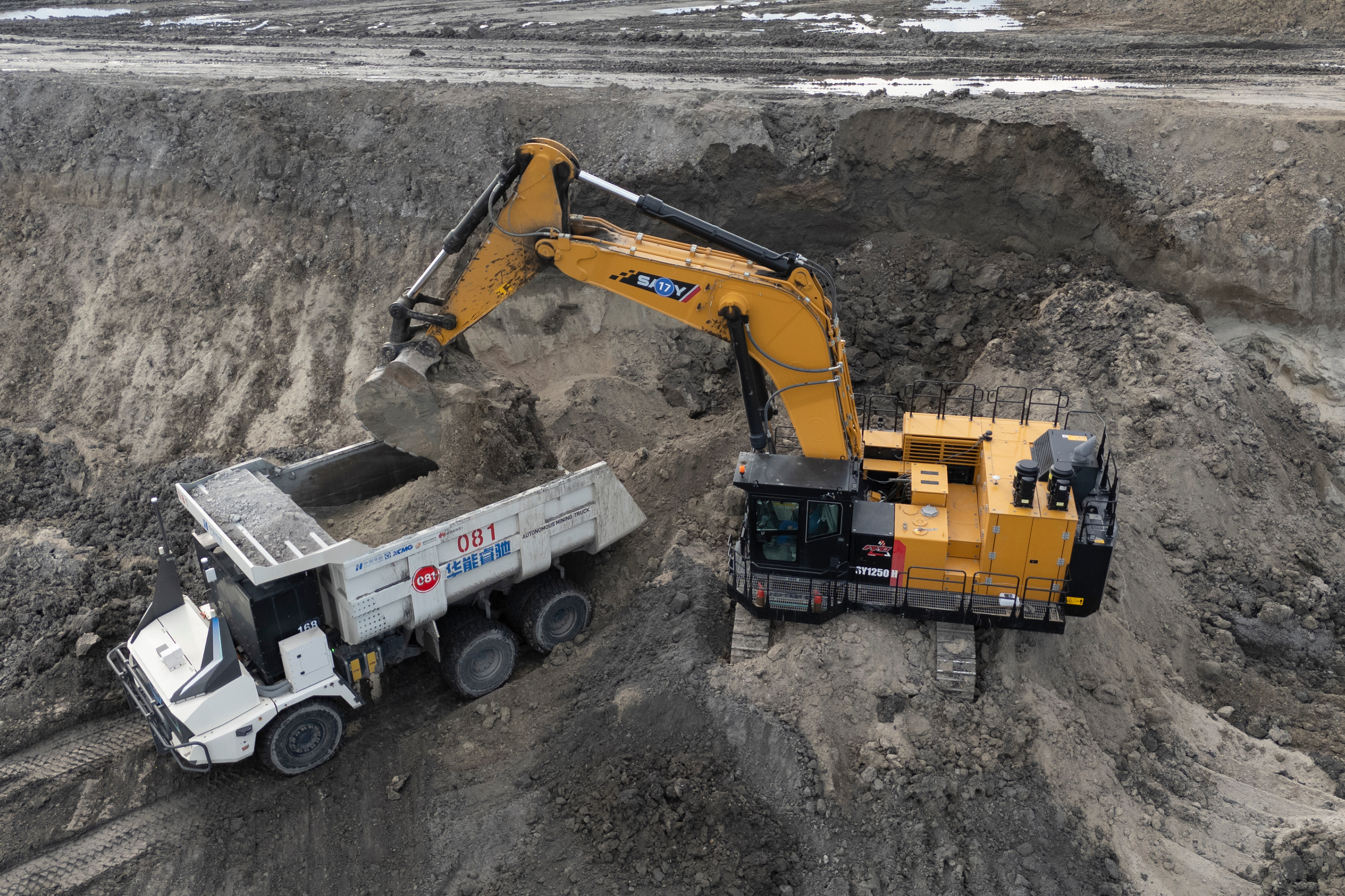 Yellow excavator loading dirt into white dump truck at construction site