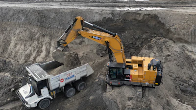 Yellow excavator loading dirt into white dump truck at construction site