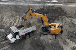 Yellow excavator loading dirt into white dump truck at construction site