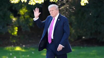 Person in navy suit and pink tie walking on green lawn, waving hand