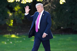 Person in navy suit and pink tie walking on green lawn, waving hand