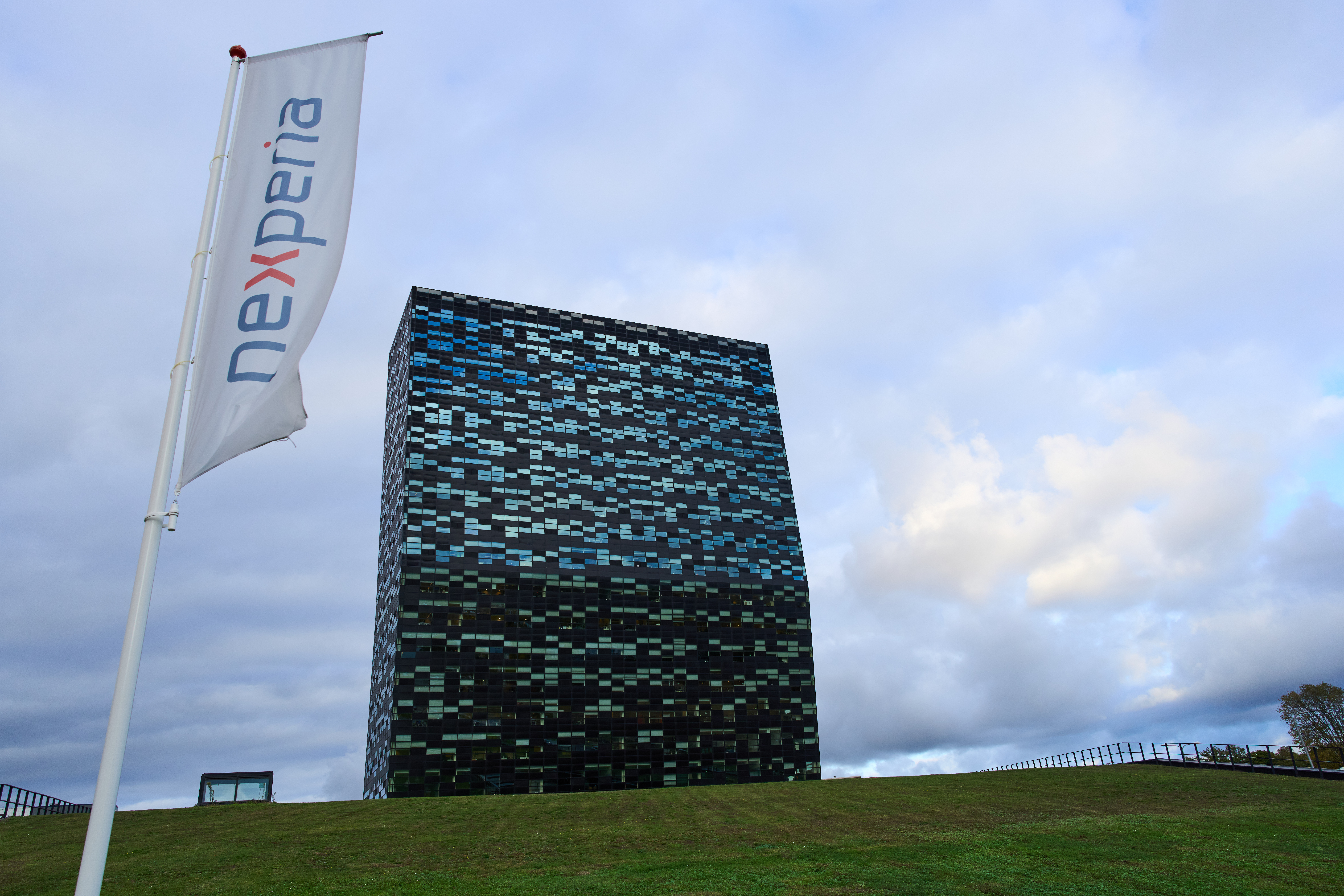 Nexperia corporate flag and modern black-blue geometric building on grassy hill