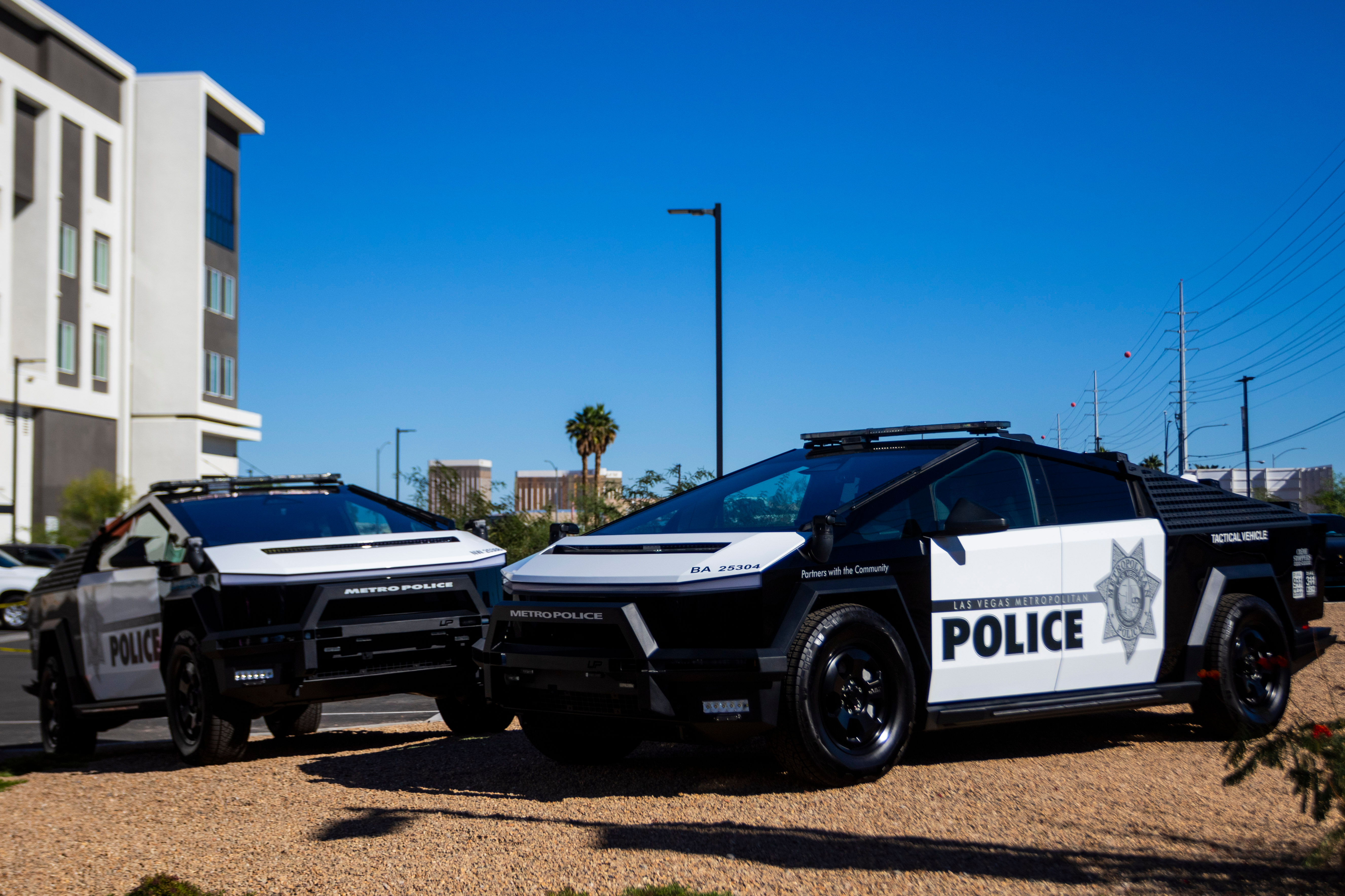 Two black and white police patrol vehicles parked on gravel with urban background