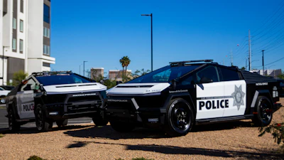 Two black and white police patrol vehicles parked on gravel with urban background