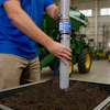 Agricultural technician testing soil sample in industrial facility near green farming equipment