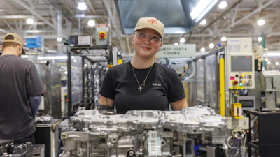 Factory worker standing near automotive engine components in manufacturing facility