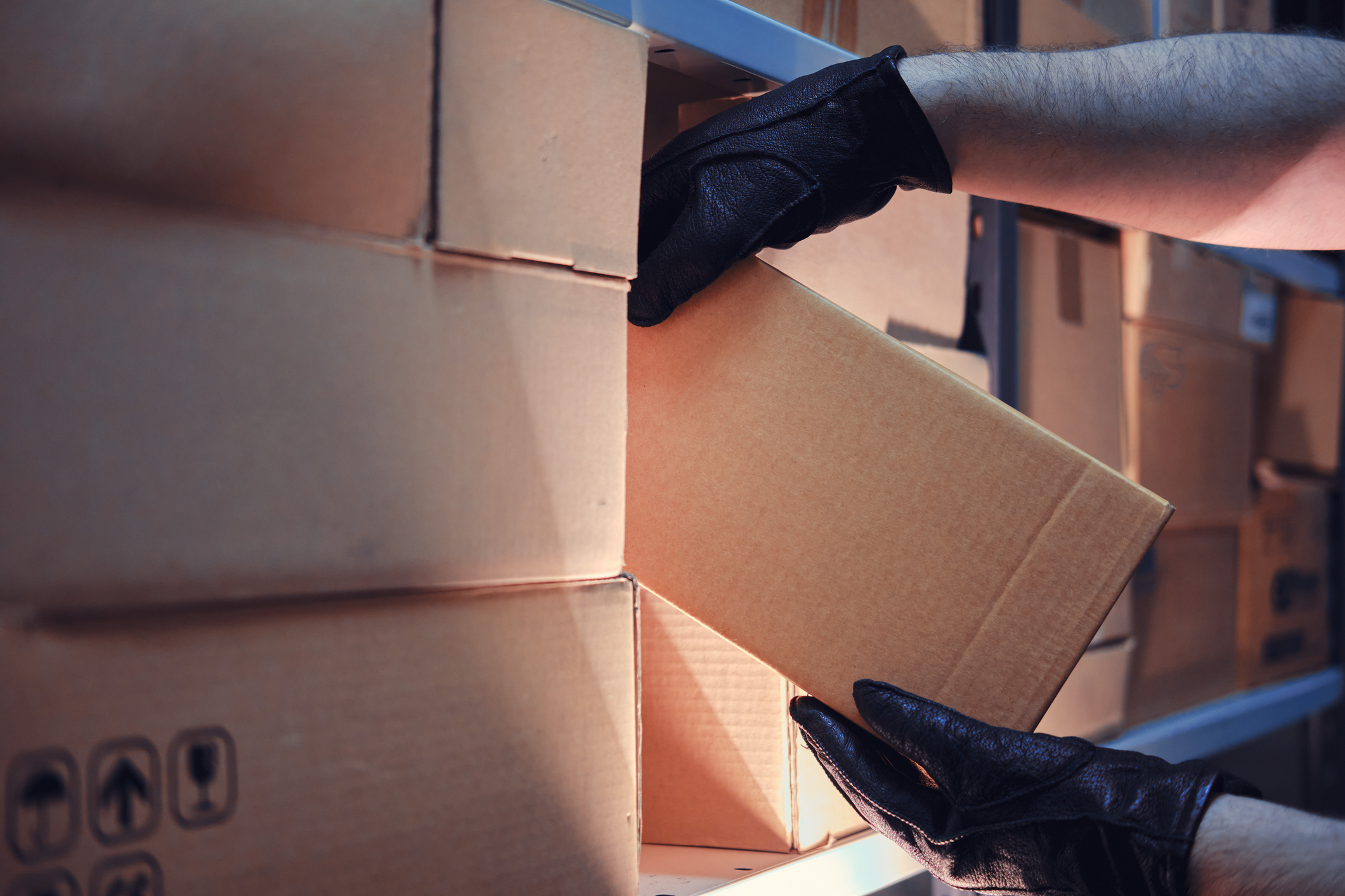Gloved hands stacking and moving cardboard moving boxes in warehouse