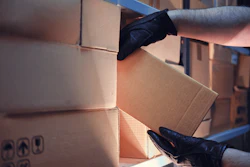 Gloved hands stacking and moving cardboard moving boxes in warehouse
