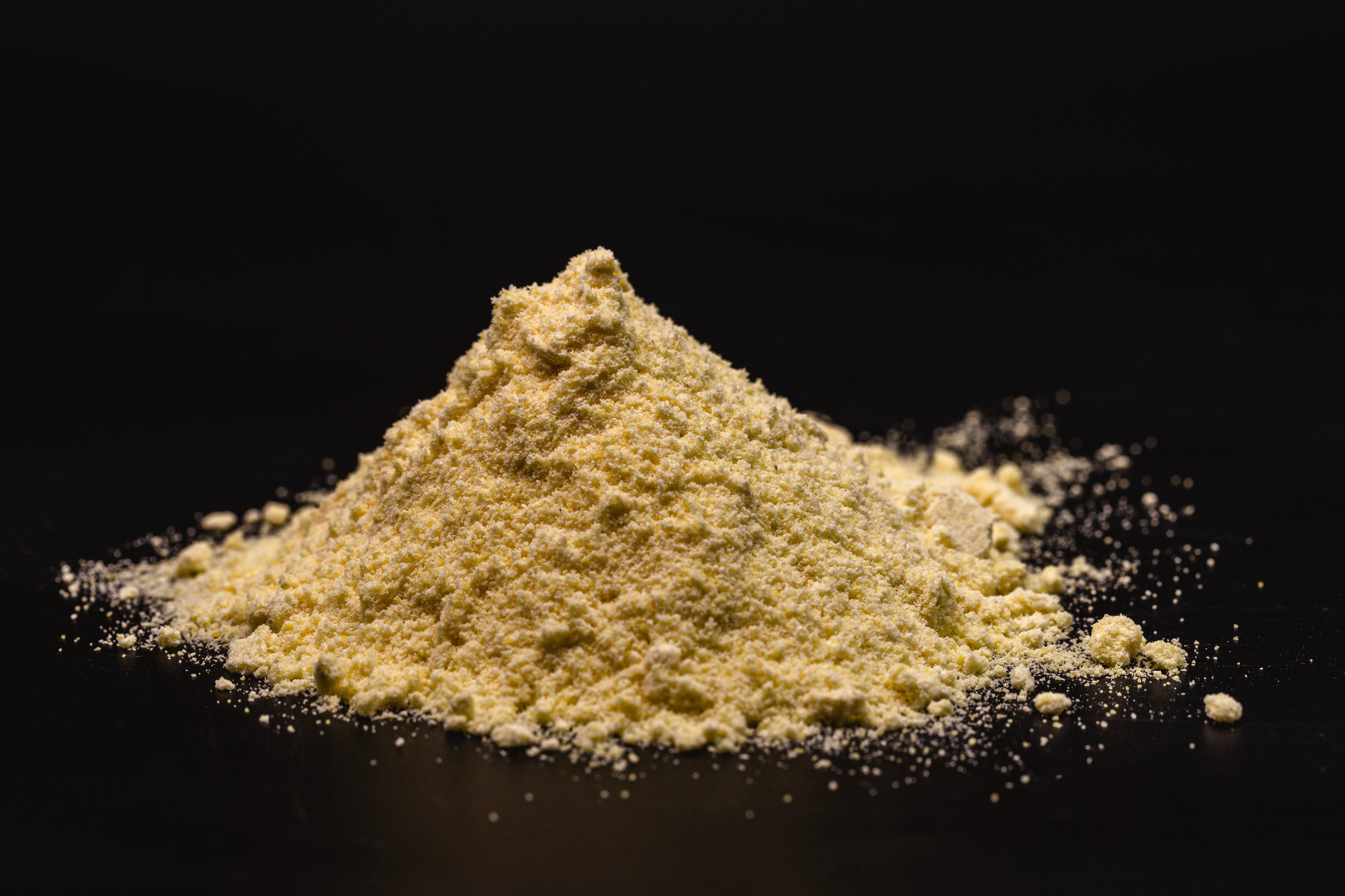 Pile of yellow ground powder with scattered granules on black background