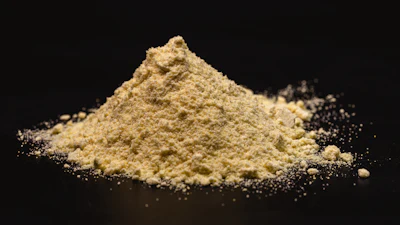 Pile of yellow ground powder with scattered granules on black background