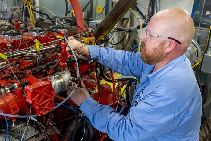 Technician in blue shirt working on a red industrial engine with complex wiring