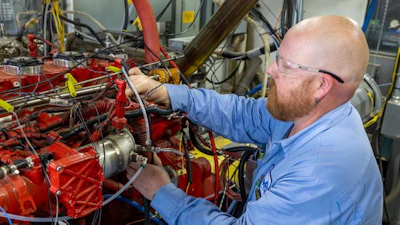 Technician in blue shirt working on a red industrial engine with complex wiring