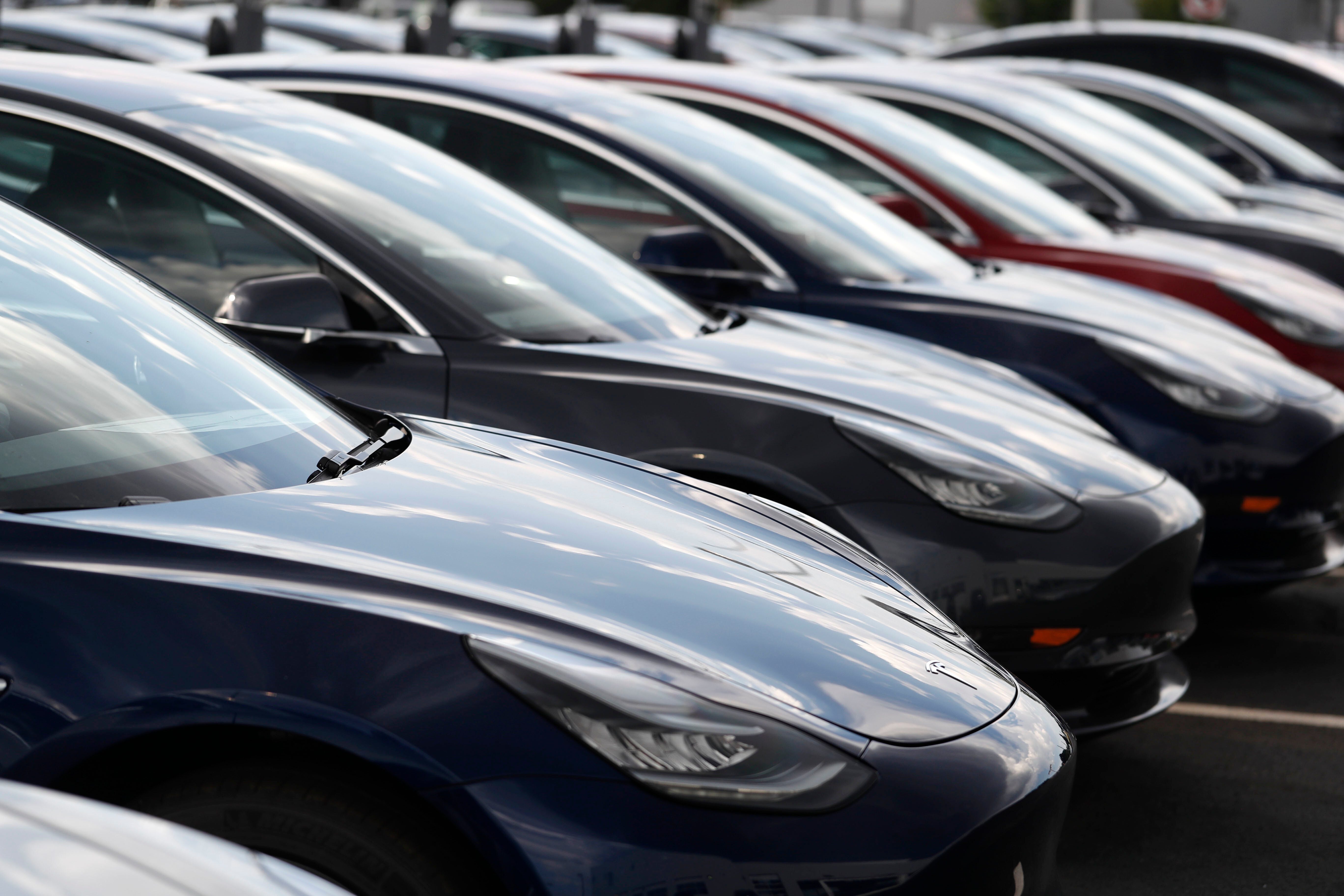 Multiple dark blue Tesla electric vehicles lined up in a parking lot