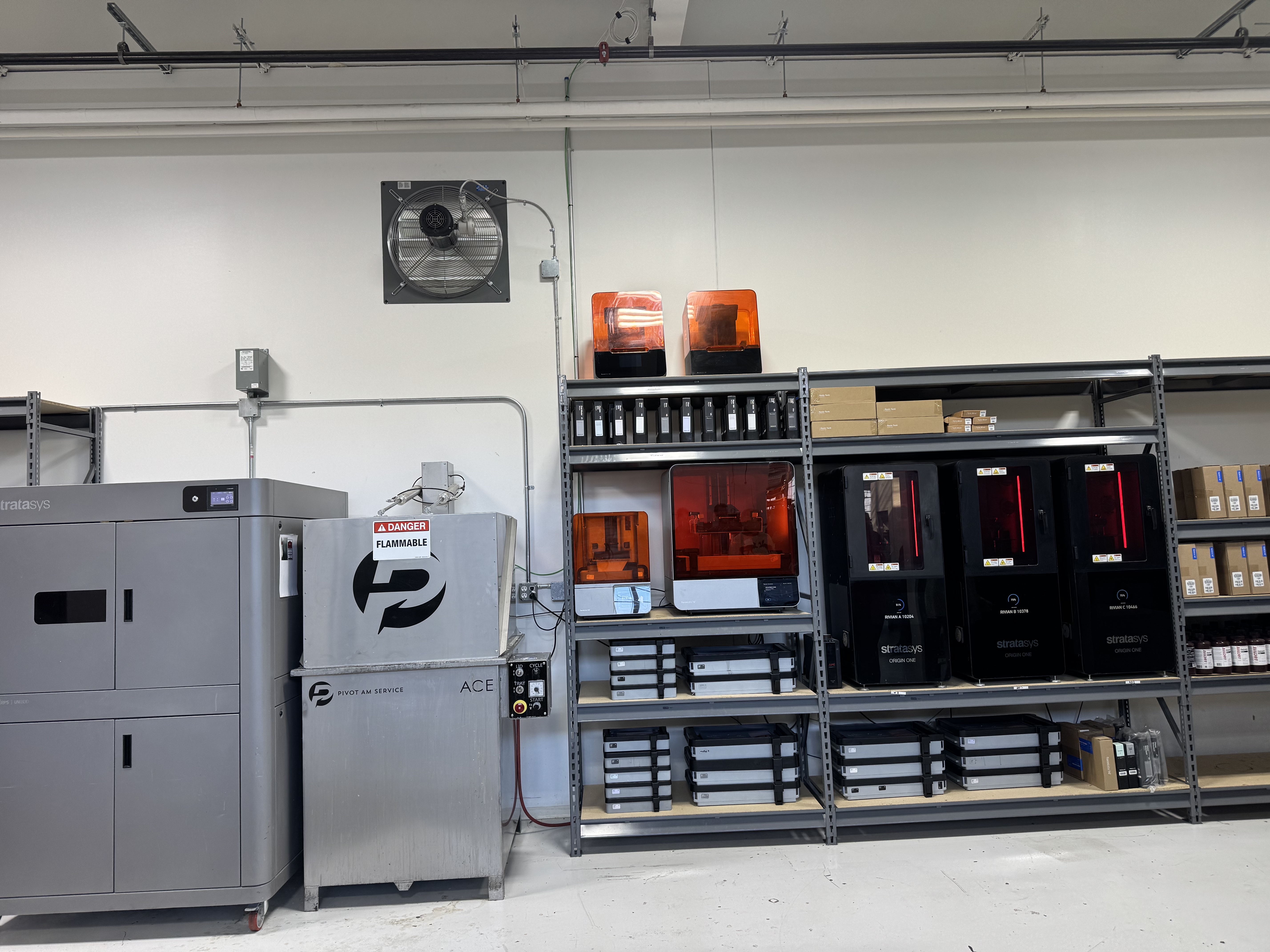 Industrial workspace with 3D printers, metal shelving, and orange safety lights