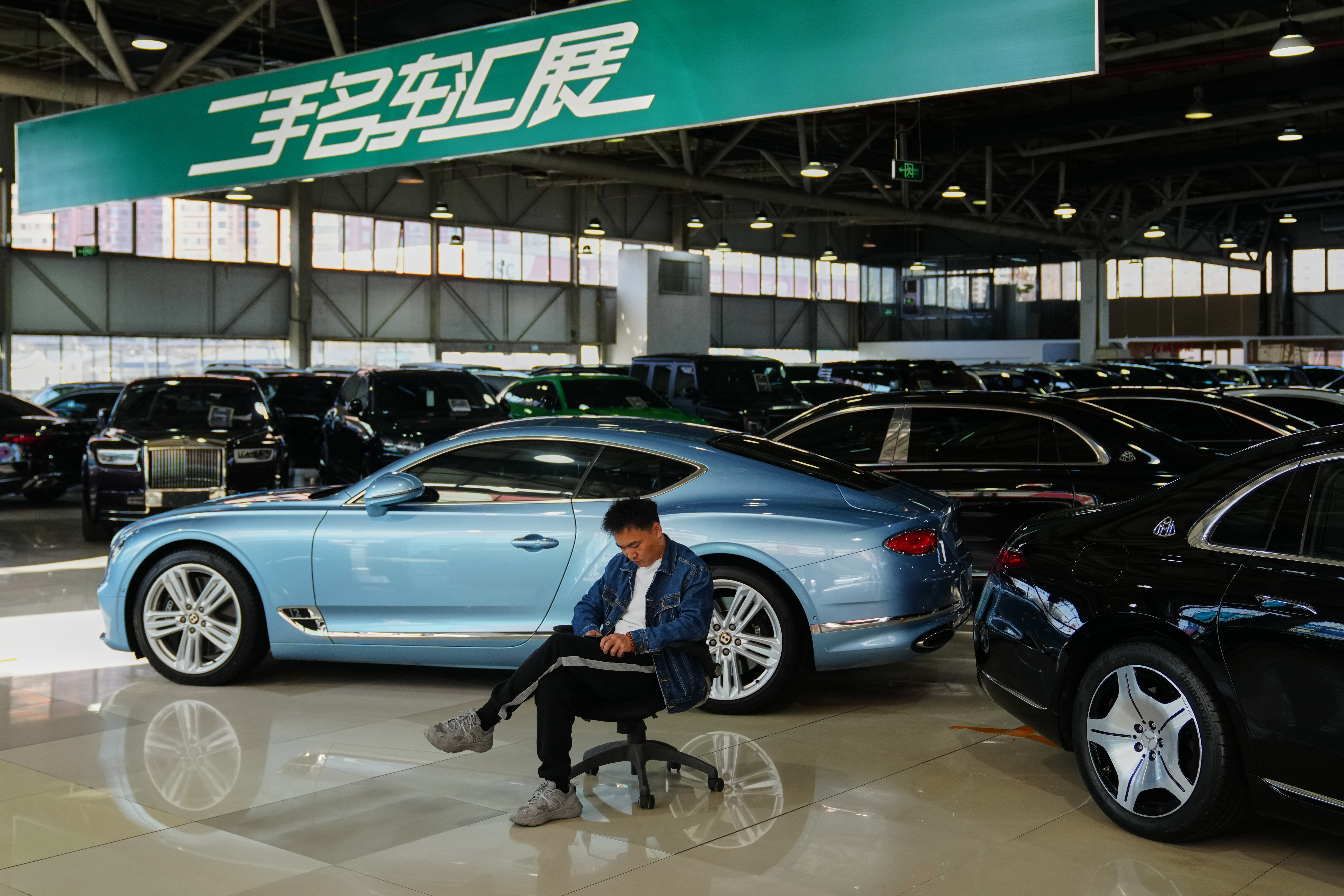 Blue luxury car in showroom with person sitting on office chair