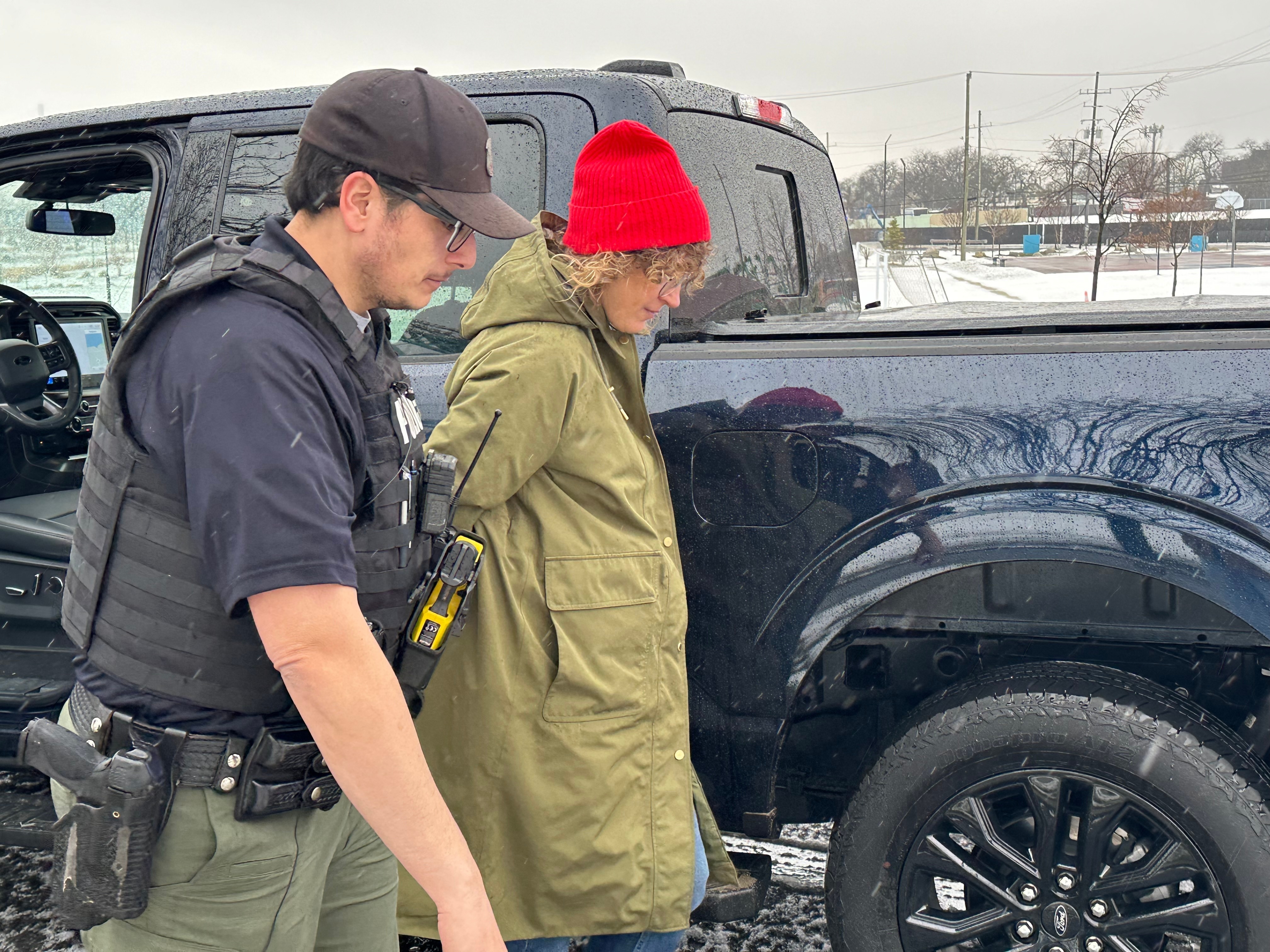 Law enforcement officer assisting person in winter clothing near black truck