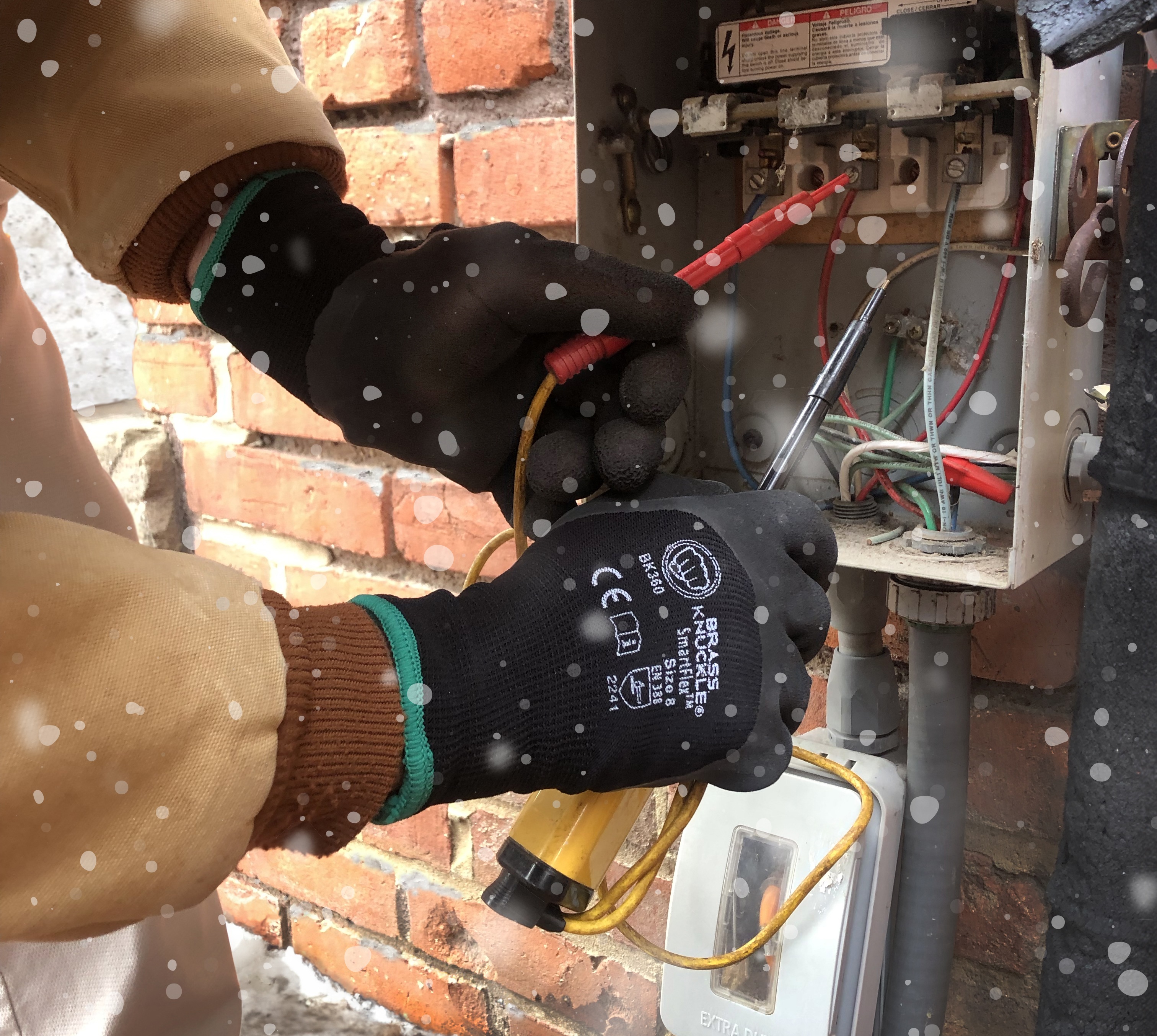 Technician wearing protective gloves repairing electrical panel near brick wall