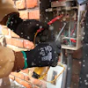 Technician wearing protective gloves repairing electrical panel near brick wall