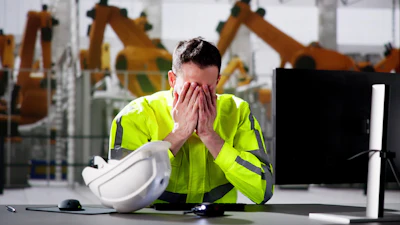 Exhausted industrial worker in safety vest covering face near hard hat