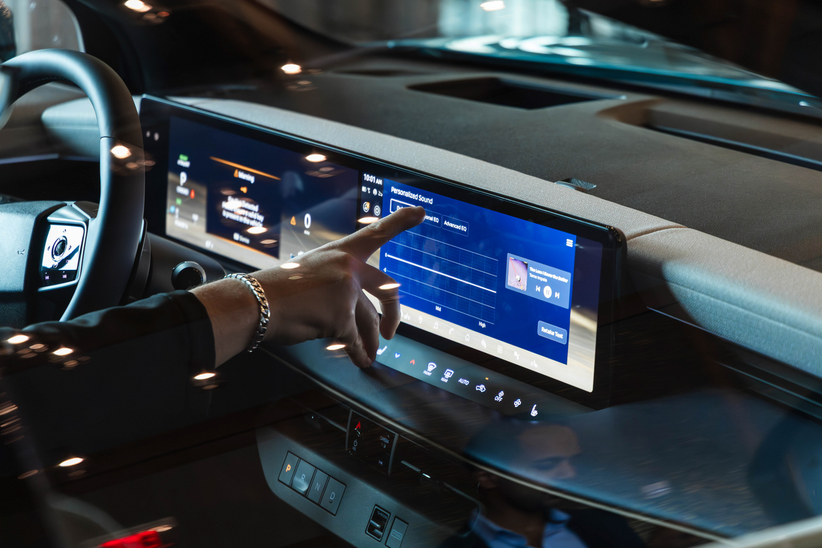 Car dashboard with digital touchscreen displaying blue interface and hand touching screen