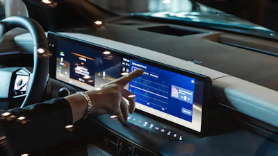 Car dashboard with digital touchscreen displaying blue interface and hand touching screen