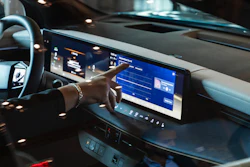Car dashboard with digital touchscreen displaying blue interface and hand touching screen