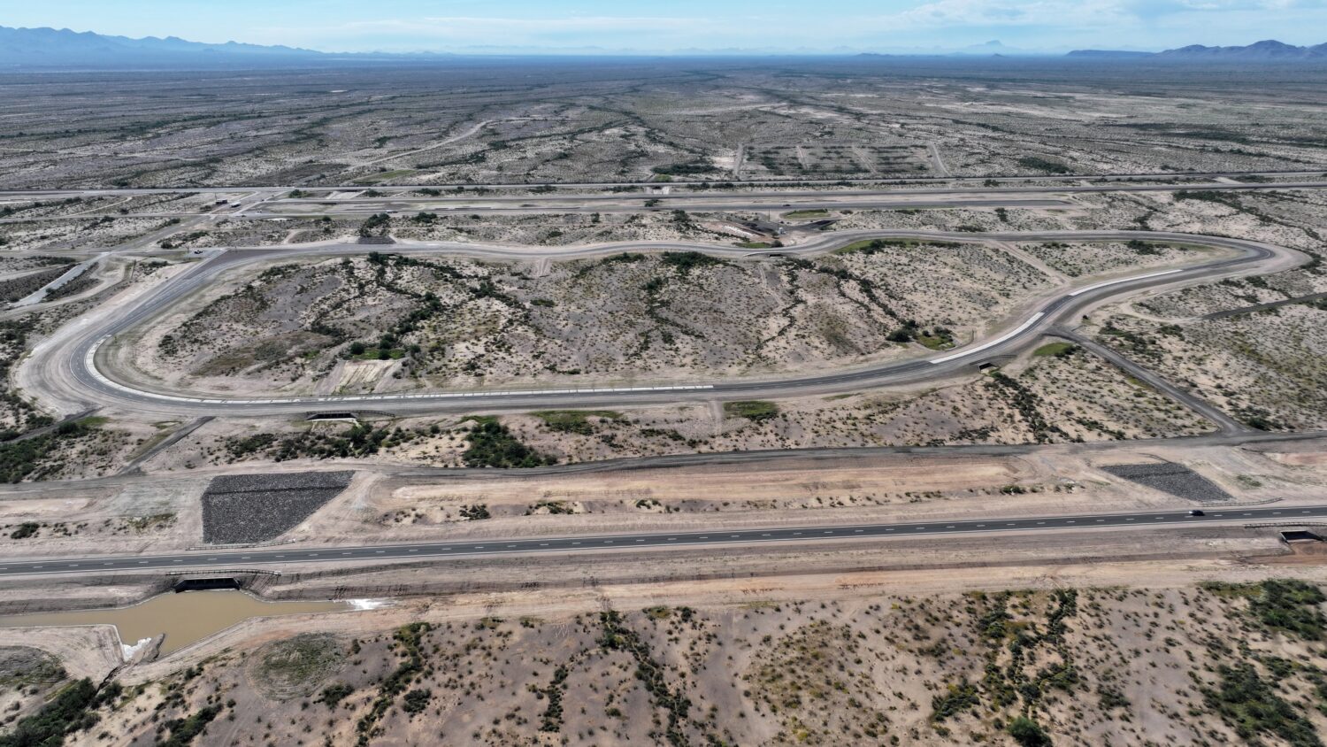 Aerial view of curved mountain road through rocky desert landscape with mountain range
