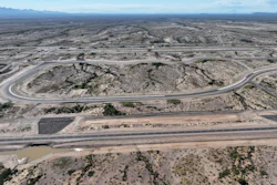 Aerial view of curved mountain road through rocky desert landscape with mountain range