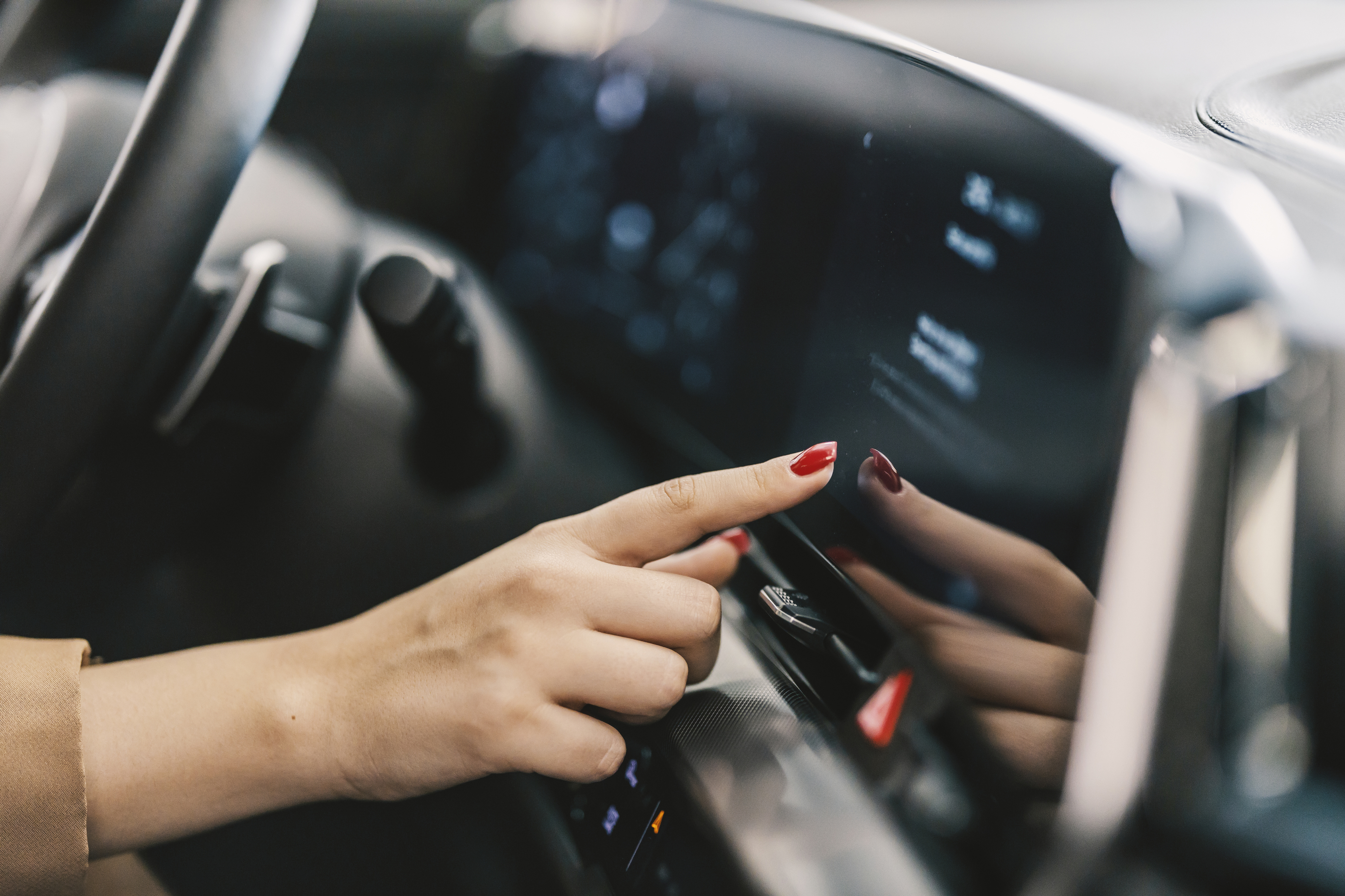 Hand with red nail polish touching car dashboard touchscreen