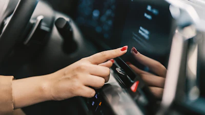 Hand with red nail polish touching car dashboard touchscreen
