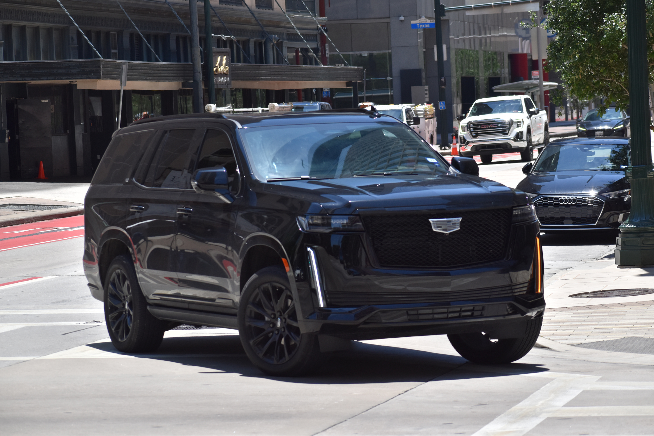 Black Cadillac SUV driving on city street with other vehicles in background