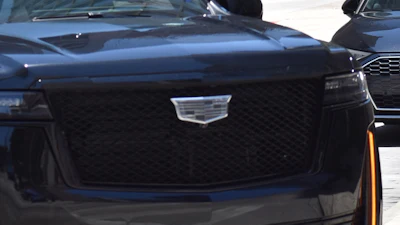 Black Cadillac SUV driving on city street with other vehicles in background