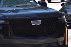 Black Cadillac SUV driving on city street with other vehicles in background