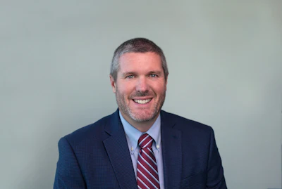 Smiling professional in navy suit and red striped tie against neutral background