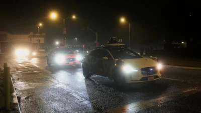 Vehicles driving on wet, rainy street at night with street lights illuminating road