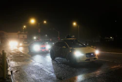 Vehicles driving on wet, rainy street at night with street lights illuminating road